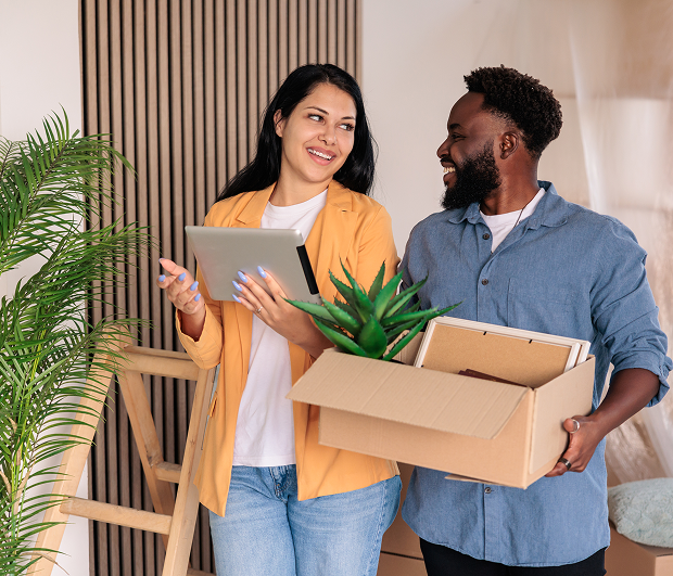 Couple with box and tablet smiling indoors.